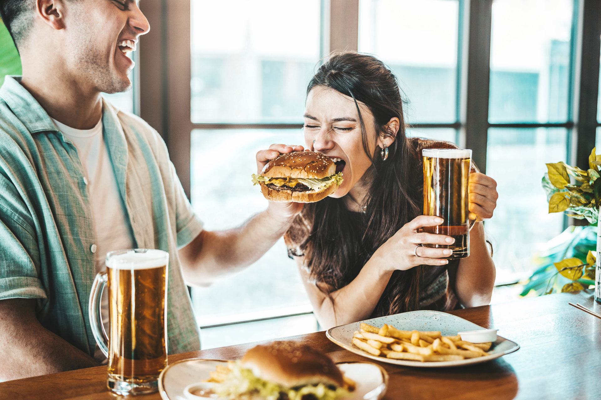 Happy couple eating burger sitting at pub restaurant